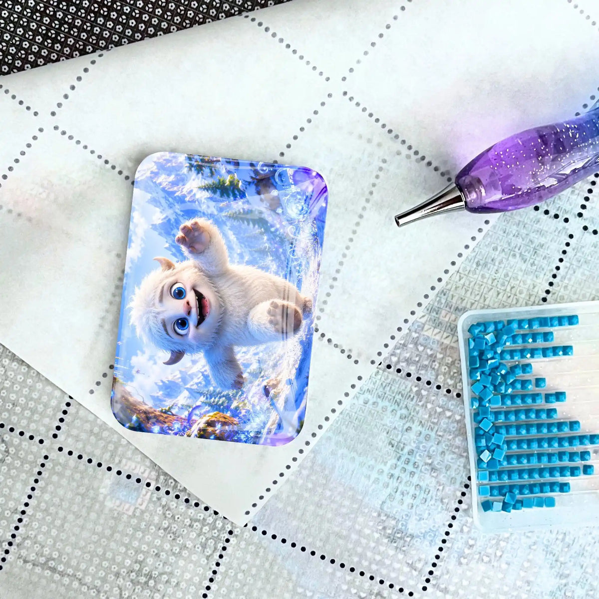 Cover Minder Mitten ins Abenteuer mit Yeti auf Diamond Painting Leinwand neben blauem Zubehör-Schiffchen